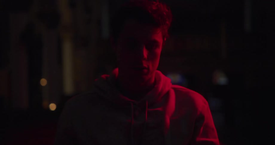 Young man wearing a hoodie stands on the streets at night under passing red lights
