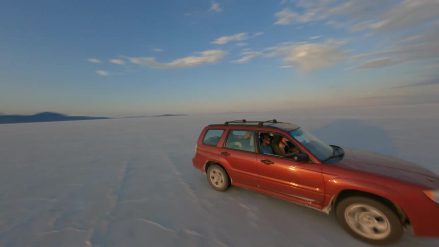 An aerial view of a red vehicle driven by one person and occupied by a passenger driving through the desert