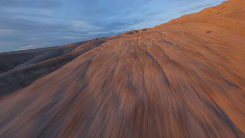 Drone casts shadow across badlands as it flies toward person standing on stone hill