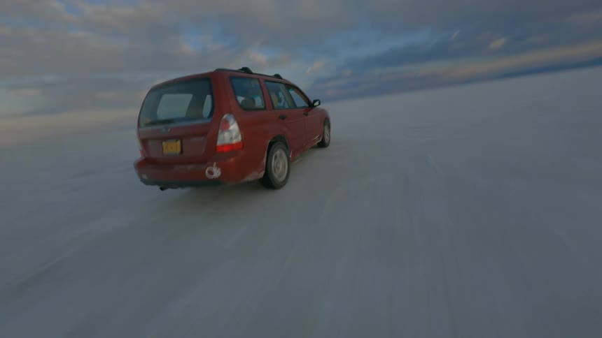 Aerial view of a red vehicle driving on the flat landscape of a desert at sunset