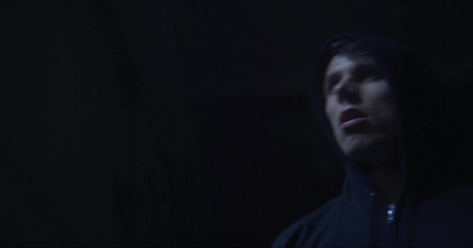 Close up of the face of a young man wearing a hoodie looking out the window on a dark room