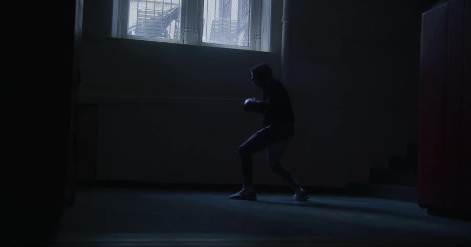 A man wearing a hoodie air boxing in a window lit room