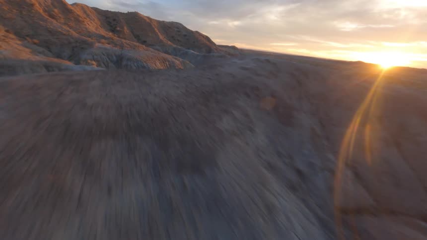 Point of view of an aerial object flying above a rocky area at sunset above canyons in the desert at high speed