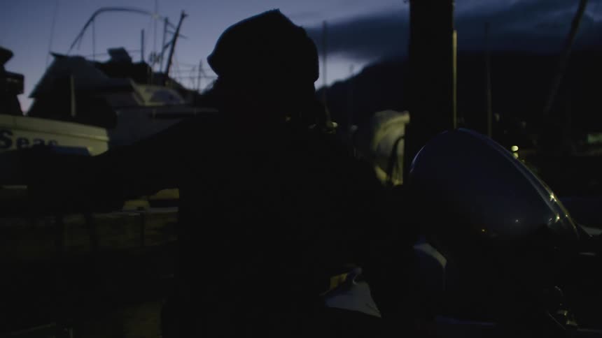 A man is sitting in a small boat near the dock as he moves the motor and holds a rope