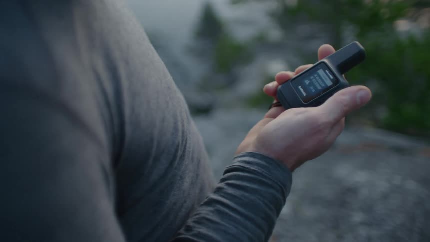 Man pulls device from pocket and check screen while standing on rock outdoors