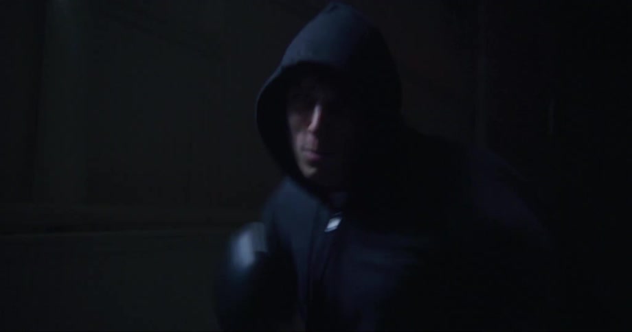 Boxer wearing hoodie shadowboxes in dimly lit area