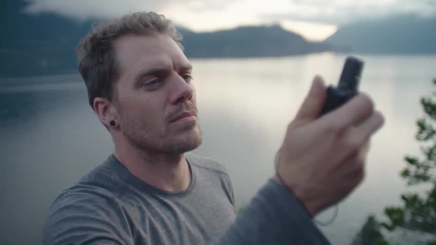 Man holds a device searching for signal in front of a lake in the mountains