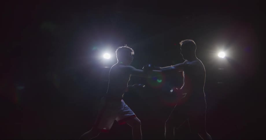 Silhouette of two men boxing on a dark room under spotlights