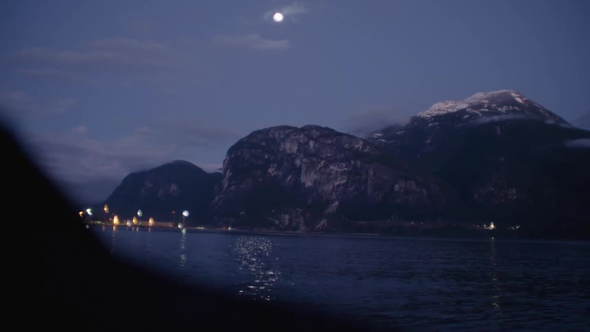 A lake reflecting a large mountain in the distance near a lighted town