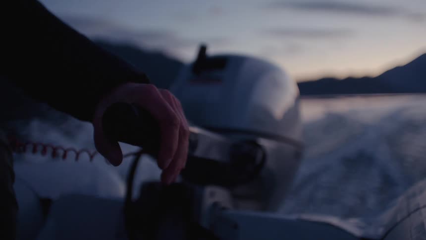 A man is sitting in a small boat holding a lever on the motor as he sails