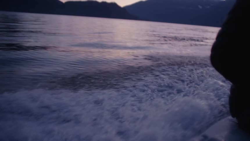 On person riding a boat at sunrise on a large body of water mountains in the distance