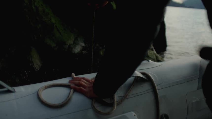 Man exits boat and climbs onto rocks to tie mooring line to rope from promontory