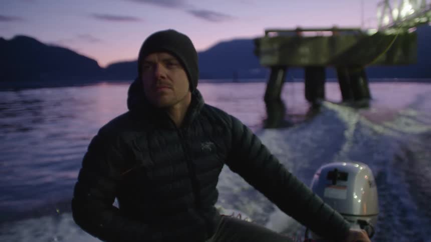 A man rides in the back of a motorboat while holding onto the motor on the ocean