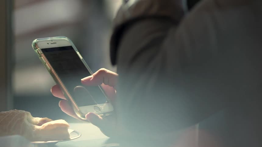 A man drinking coffee in a cafe is holding a cellphone