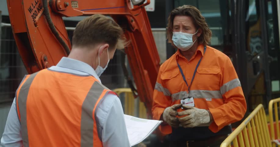 Two construction workers speak to each other outside by a railing