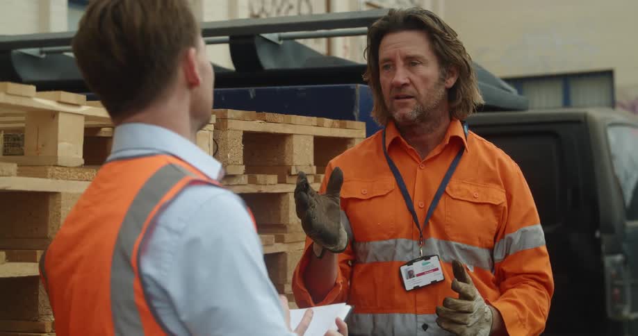 Two coworkers chatting outside of a building next to wooden pallets
