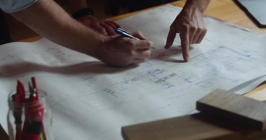 Two people consult over blueprints as one makes modifications