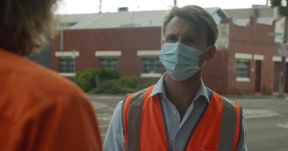 A pair of workers in reflective safety clothing speak together outdoors