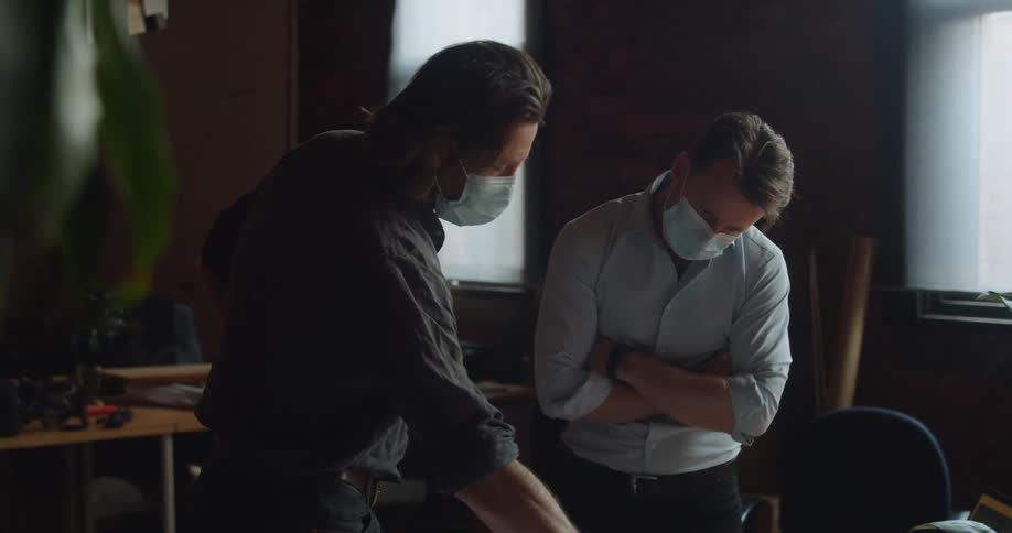 Two men discuss a blueprint spread out on a wood desk in an office