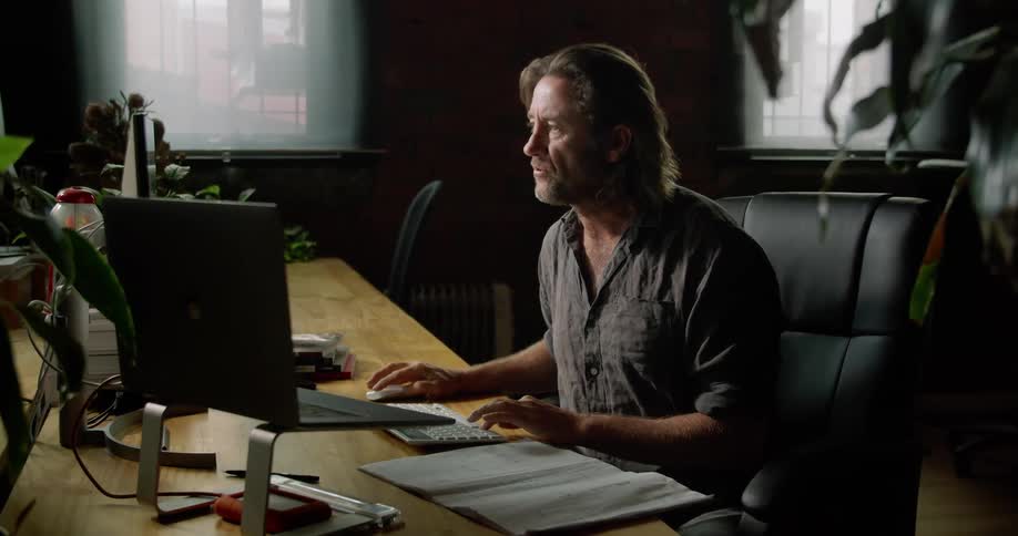 A man sits at a desk and appears to be talking to a computer