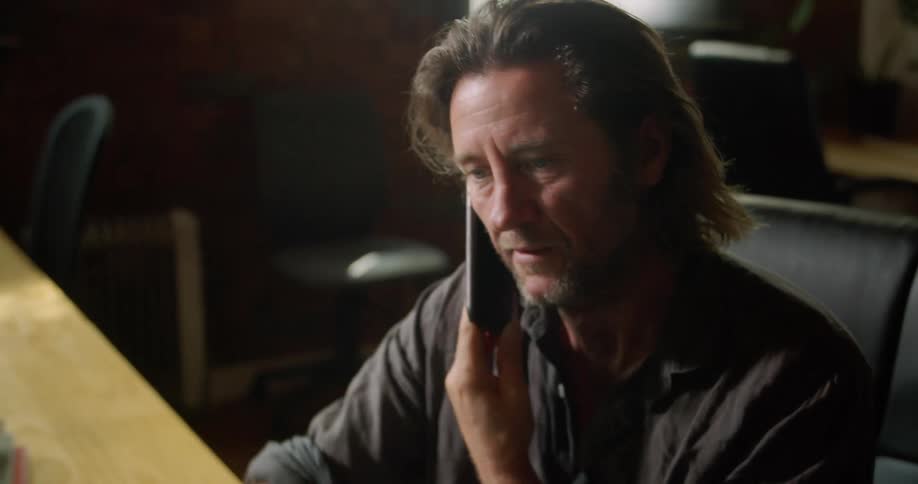 A man sitting at a desk talking on a smart phone in front of a laptop