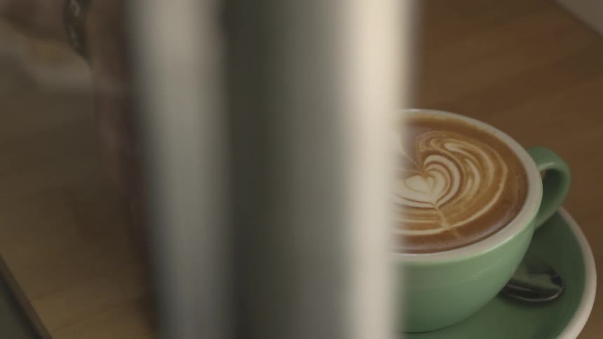 Person pushing a saucer that has a decorative coffee drink in it