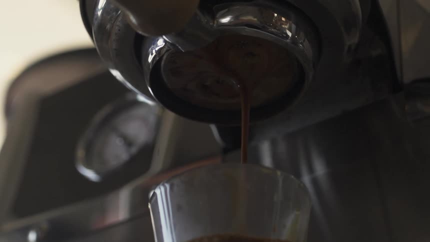 Coffee drips from an espresso machine into a container