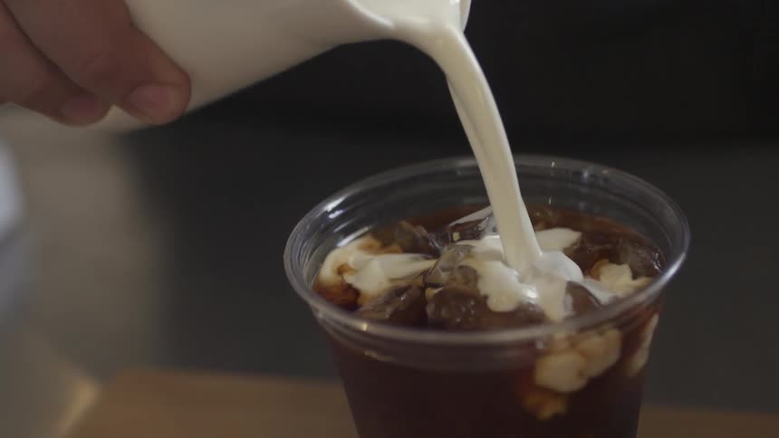 Someone pours cream into a cup of coffee
