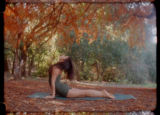 A woman with long hair is doing yoga on a yoga mat in the forest near some trees