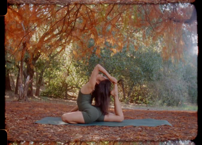 Woman with brown wavy hair red shirt and shorts does yoga on yoga mat in the autumn forest