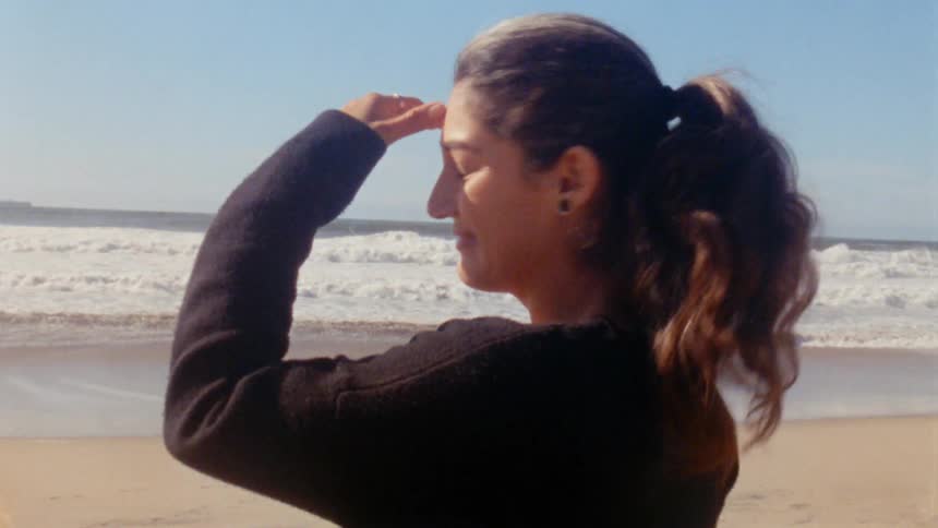 A woman turns and smiles while walking toward the ocean