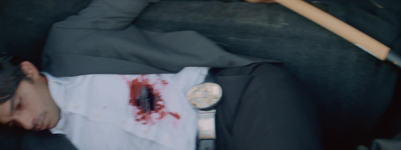 Detective inside the trunk of a car with a gun wound on his stomach laying next to a bag filled with money