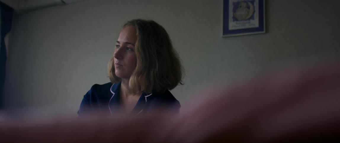 Woman with brown wavy hair and blue shirt looks into space in room thinking
