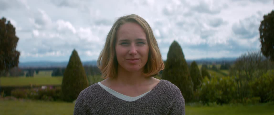 A teenage girl stands in a field and poses for a portrait