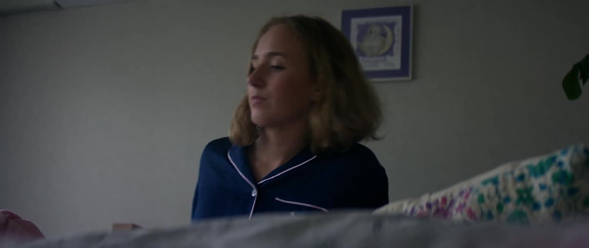 A womanin blue pajamas takes a deep breath and lays down in bed to take a nap