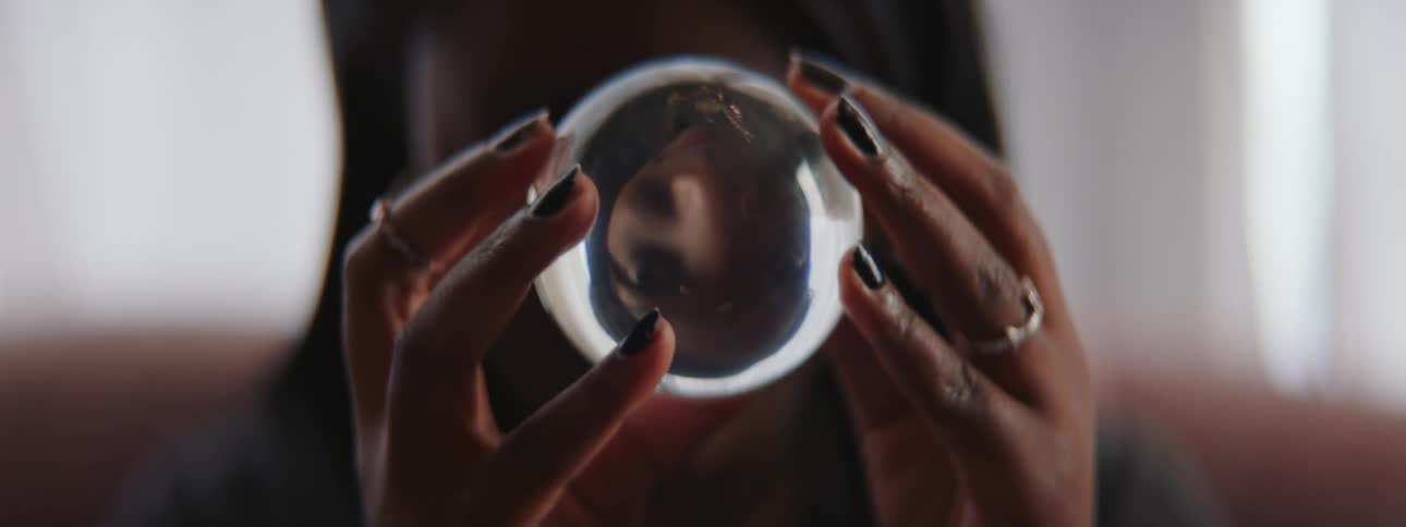 A woman holds a crystal ball in front of her face and looks in to it as she moves it around
