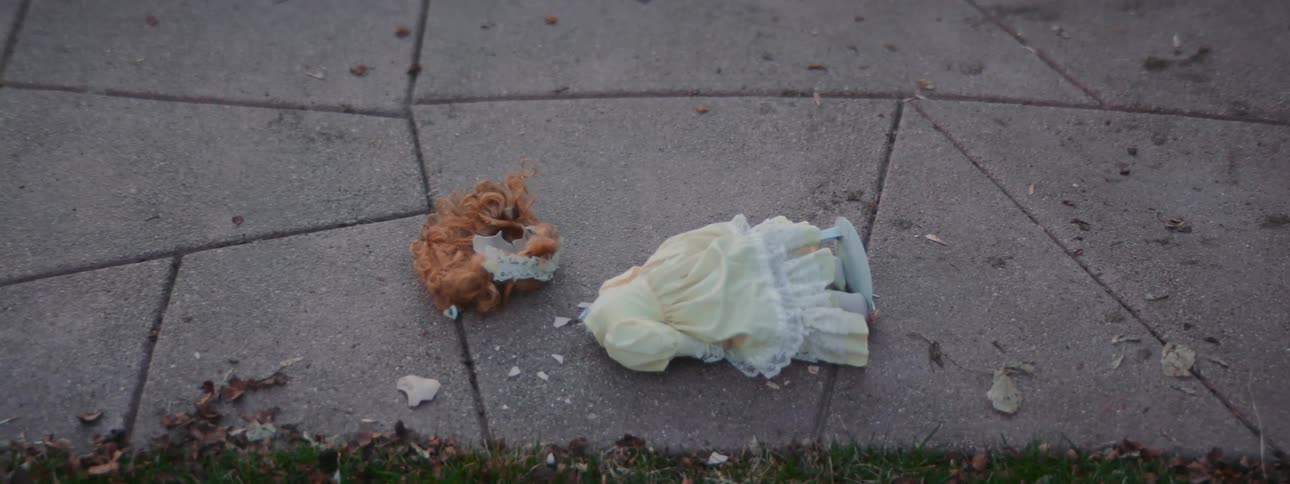 A doll falls and its head falls off and breaks on the pavement