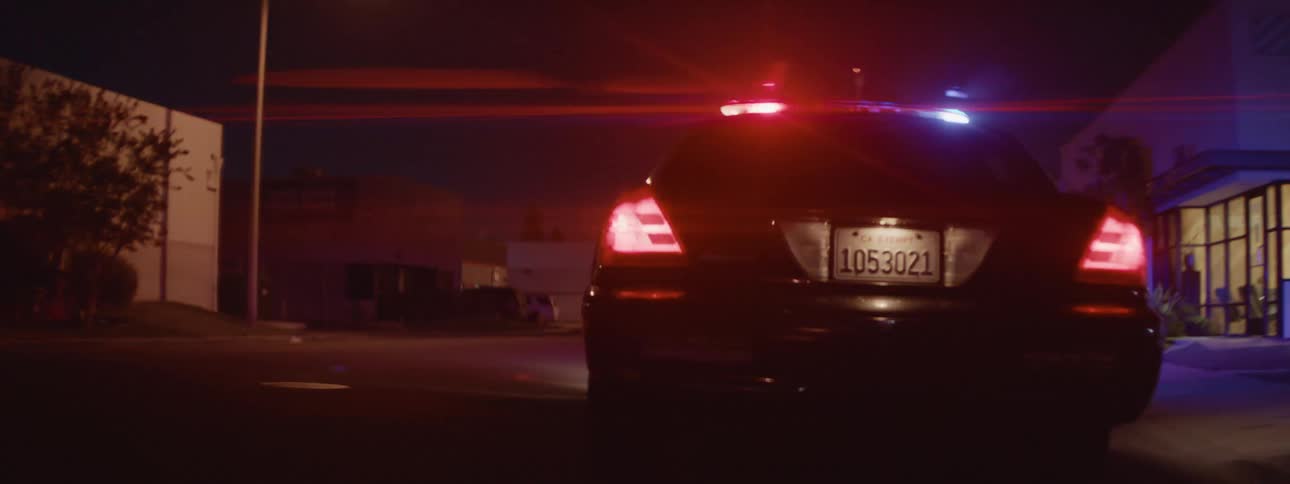 Police car with emergency lights activated chases black car in the street at night