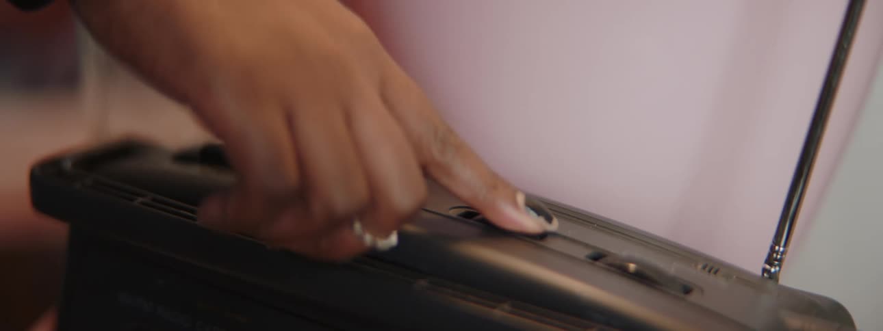 A woman uses her finger to press the button on a cassette tape player and she turns the volume dial