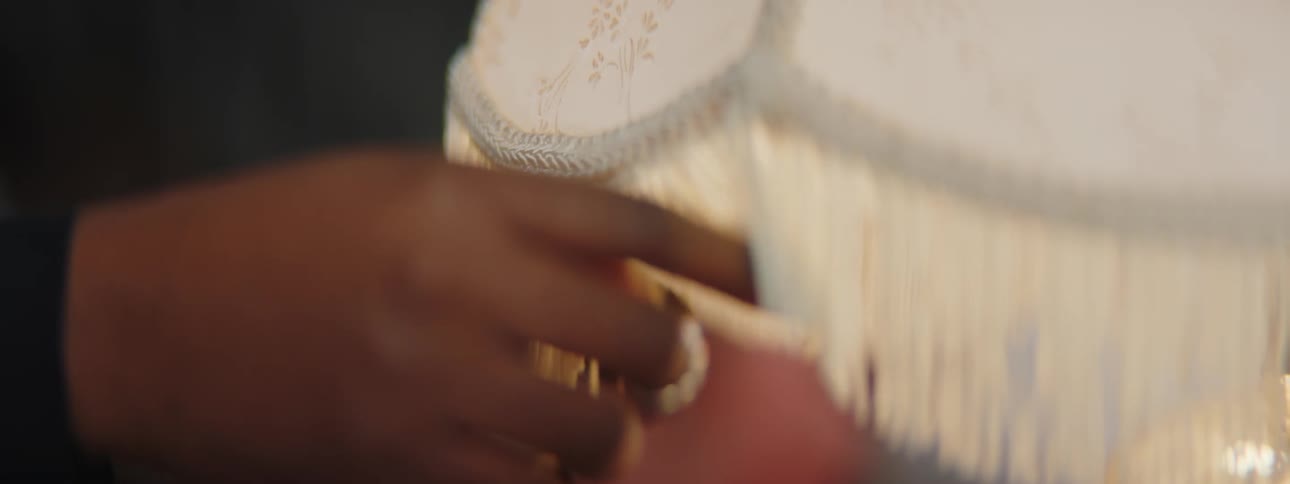 A woman runs her fingers along the fringe edge of a table lamp