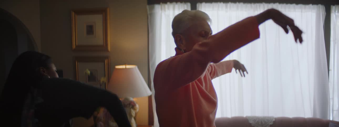 A young black woman dances with an elderly woman in her home