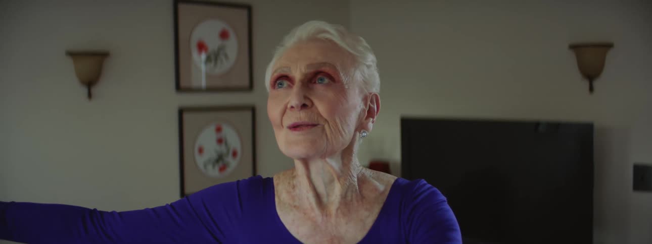 An elderly woman is standing in her living room doing tai chi exercises