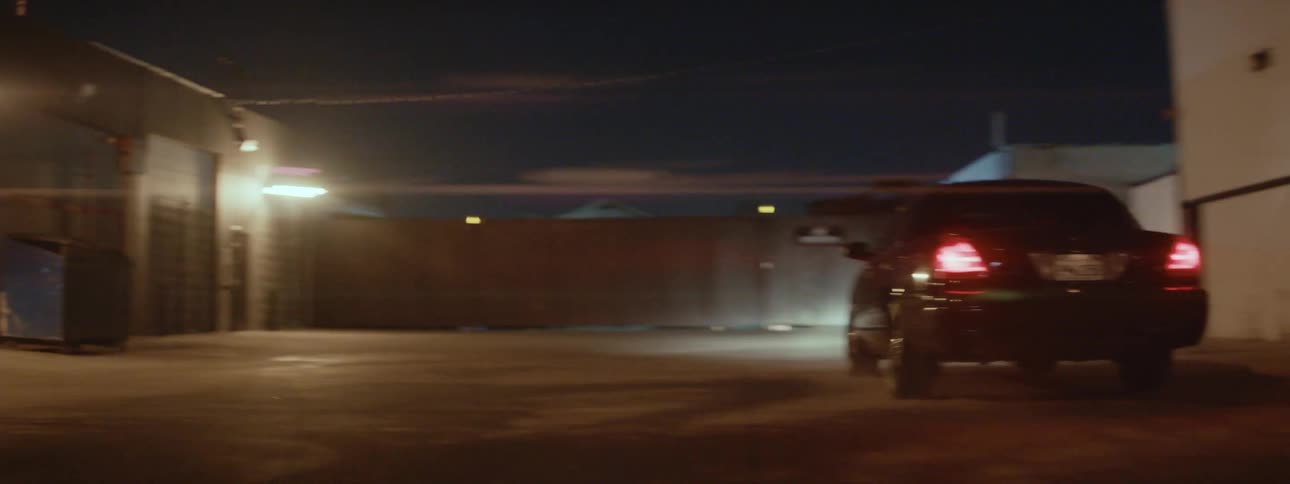 A car speeds down the alley and parks behind a dumpster