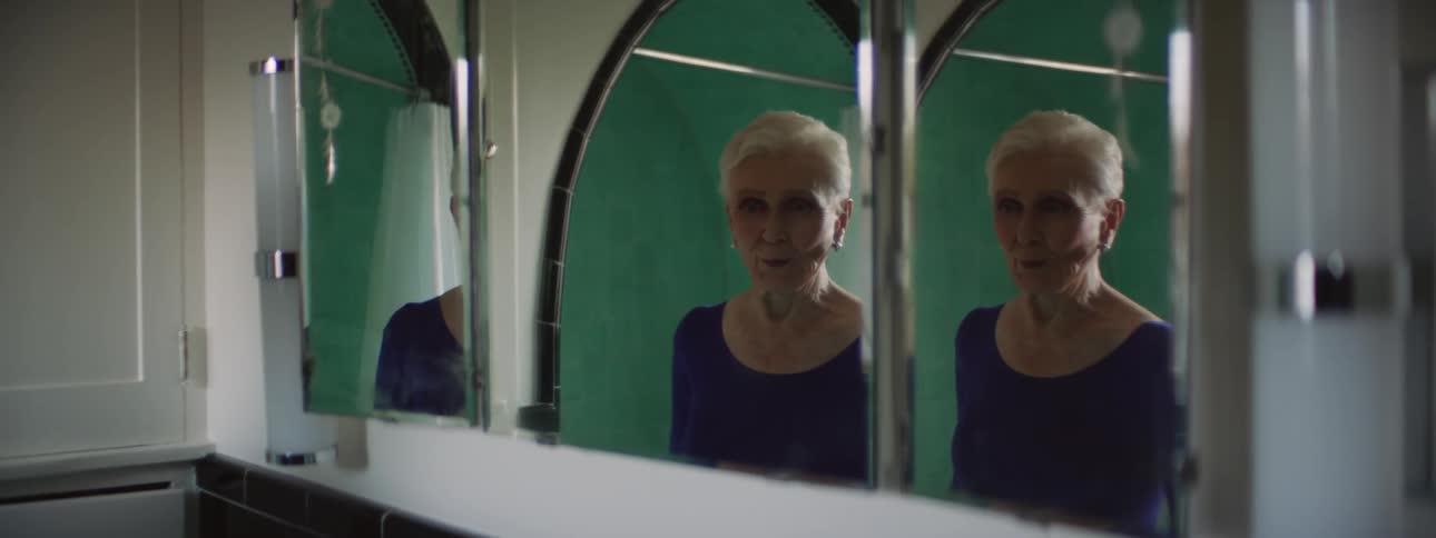 An older women dressing and standing in front of a mirror stretching and smiling