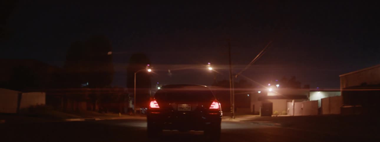 The tail lights of a black automobile glow in the darkness as it travels though a neighborhood at night