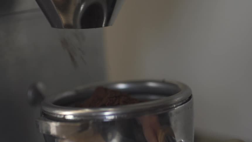 Coffee grinds shoot out of a grinder and into a container