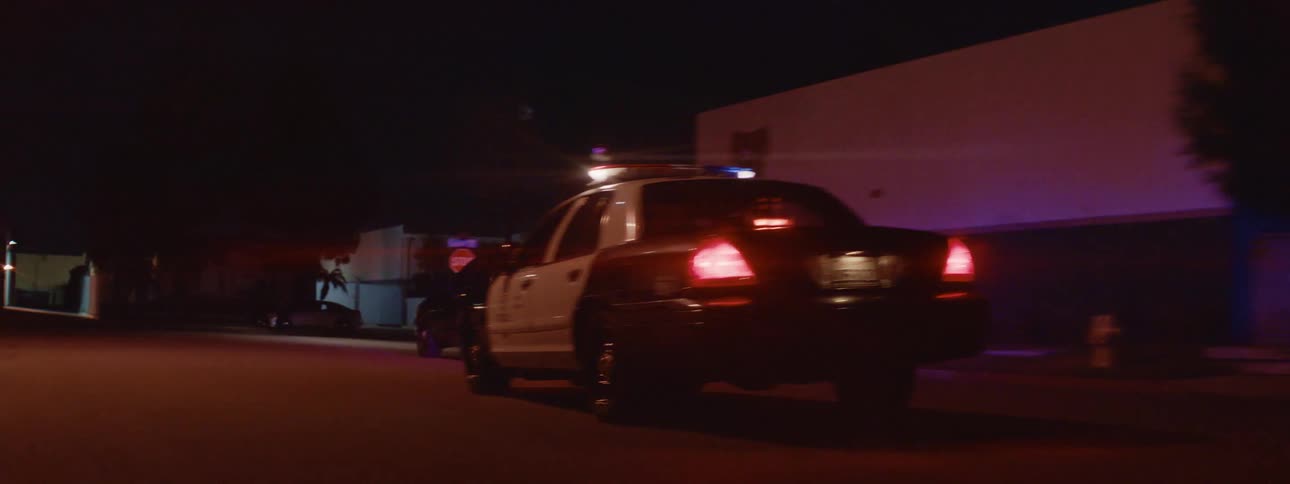 A police car is traveling with the flashers on as it follows a car through town