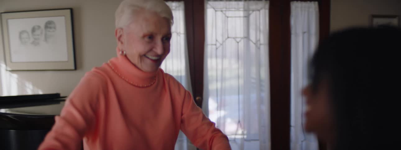 Woman and elderly woman holding hands dance happily near grand piano in room