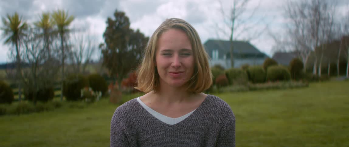 Blonde woman with gray sweater smiles at camera on the green lawn