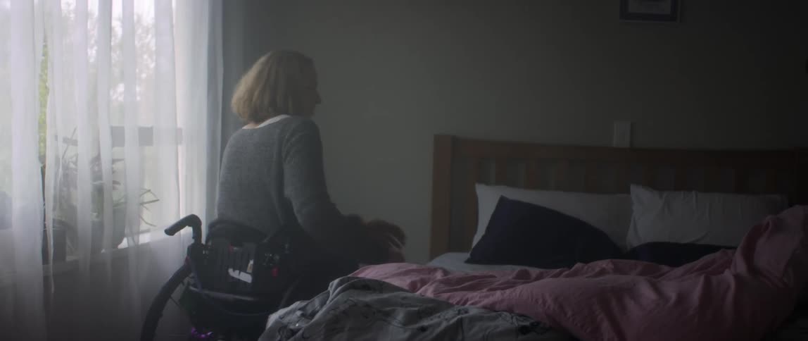 A woman in a wheelchair makes her bed